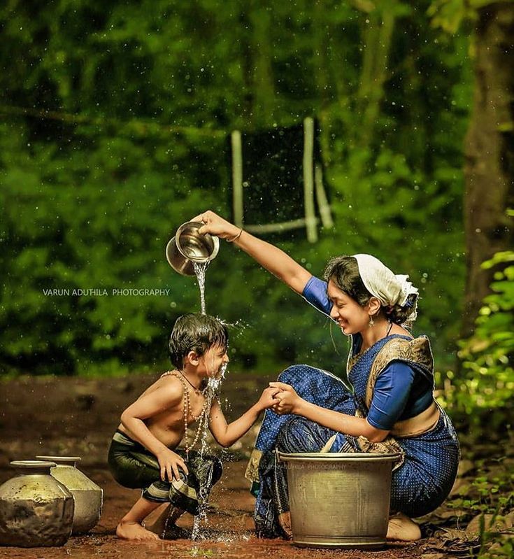 a woman and child playing with water from a faucet in a bucket while sitting on the ground