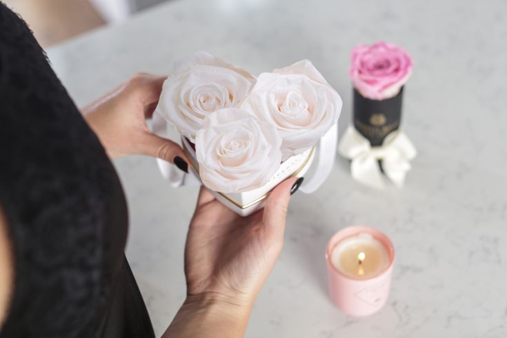 a woman holding a bouquet of roses on top of a table next to two candles