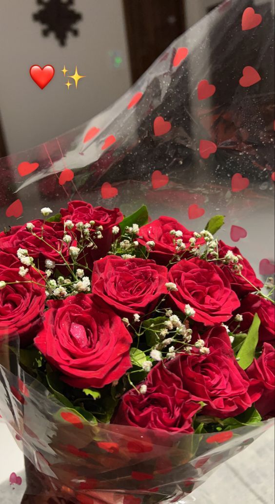 a bouquet of red roses is wrapped in clear cellophane and surrounded by confetti hearts