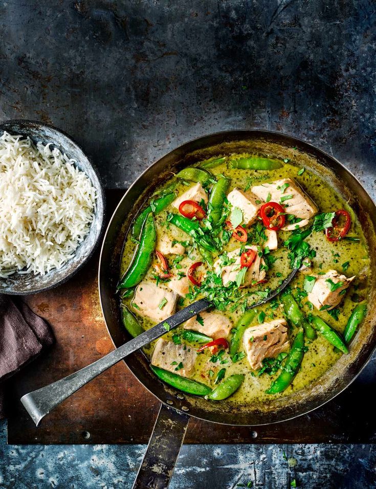 a pan filled with chicken, green beans and rice on top of a wooden table