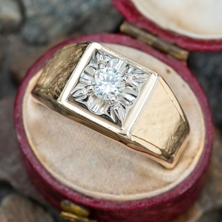 a diamond ring sitting on top of a red velvet covered box next to some rocks