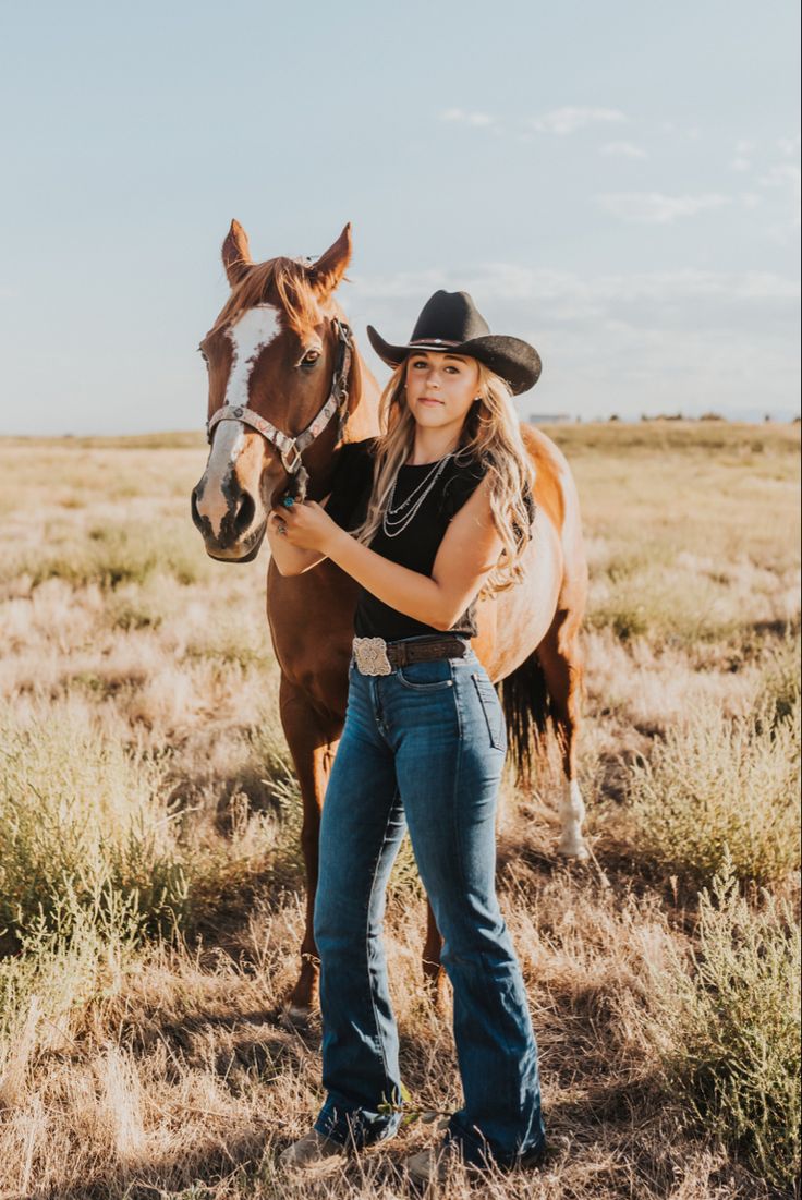 a woman standing next to a brown horse on top of a dry grass covered field