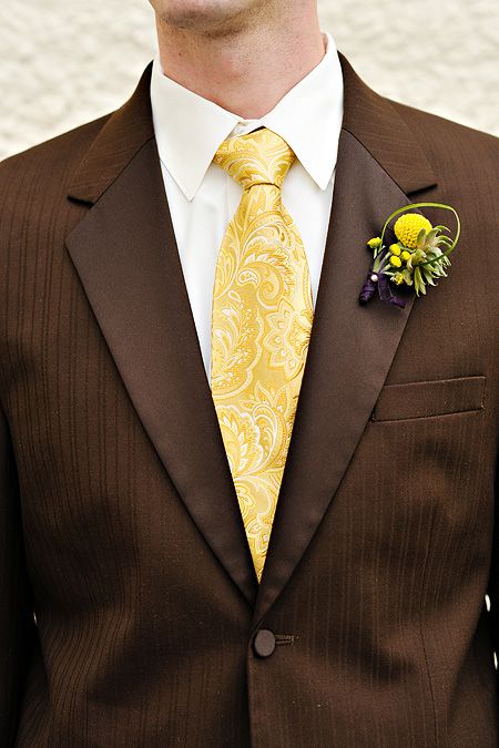 a man wearing a brown suit with a yellow tie and flower boutonniere