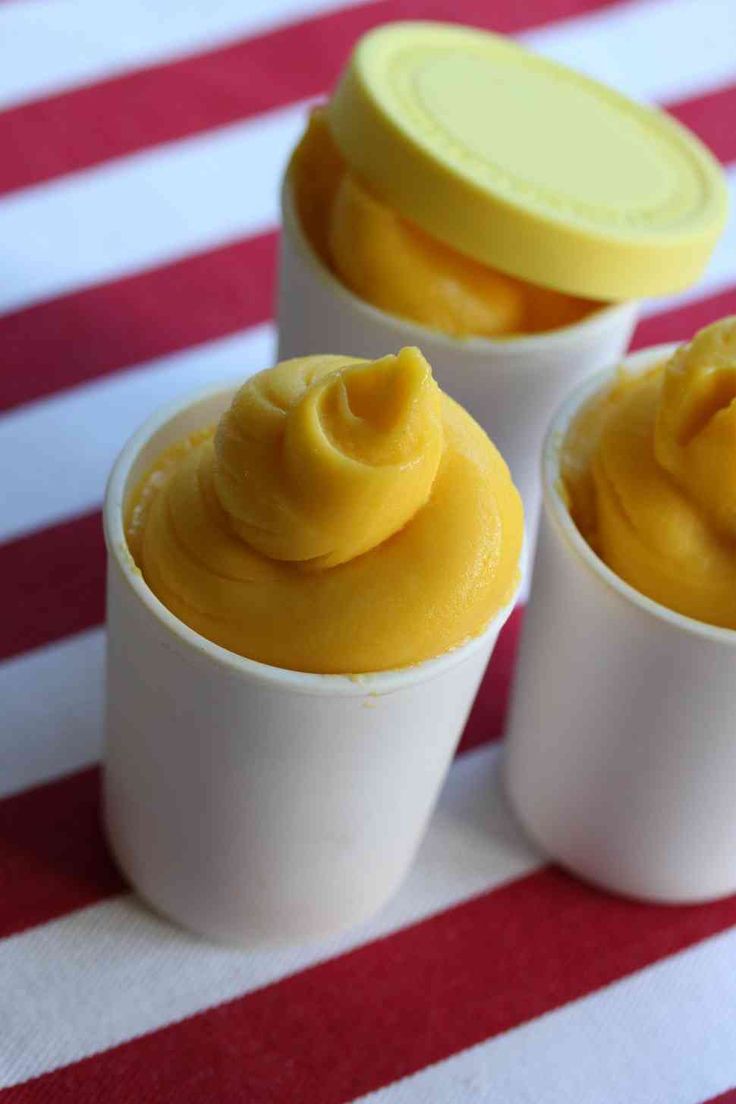 three cups filled with yellow frosting sitting on top of a red and white table cloth