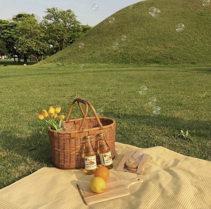 two bottles of beer are sitting on a blanket in front of a basket with lemons and oranges