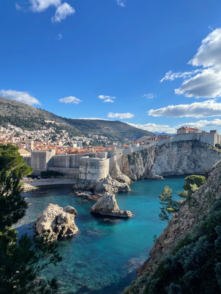 the water is crystal blue and clear with buildings on both sides, and cliffs in the background