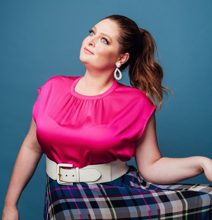 a woman in a pink top and plaid skirt sitting on a chair with her legs crossed