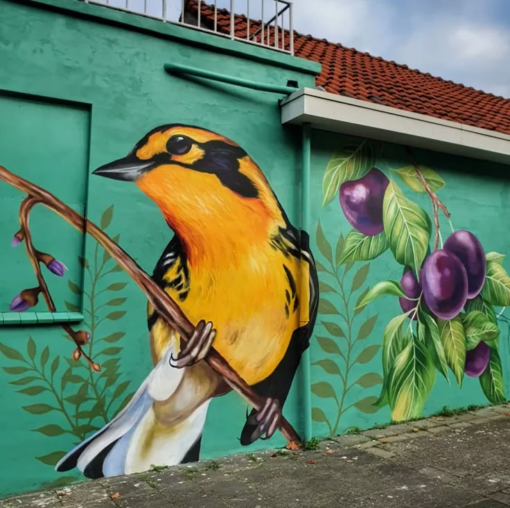 a colorful bird painted on the side of a building next to a tree and fruit