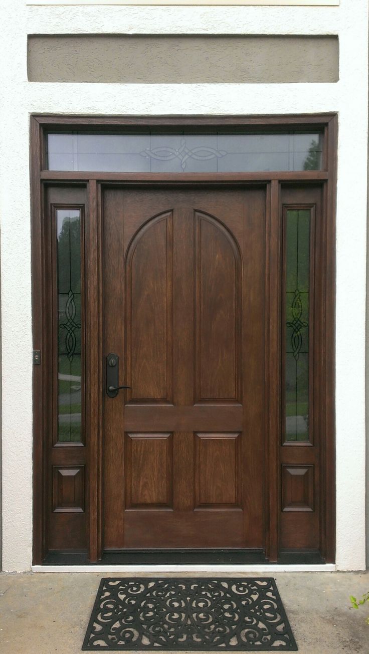 a wooden door with two sidelights and a black mat on the ground in front of it