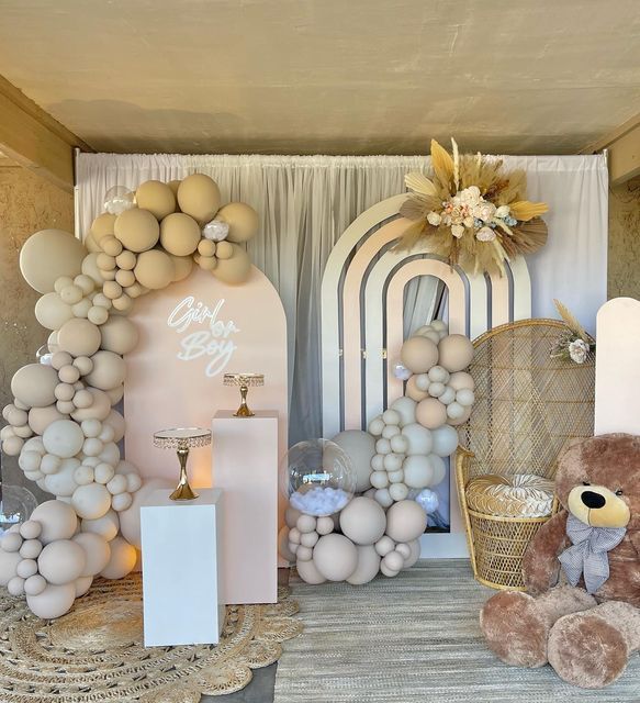 a teddy bear sitting on top of a table next to balloons and other items in front of a backdrop