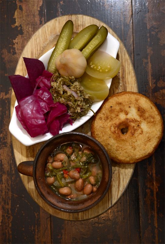 a plate with bread, beans and pickles on it next to a bowl of soup