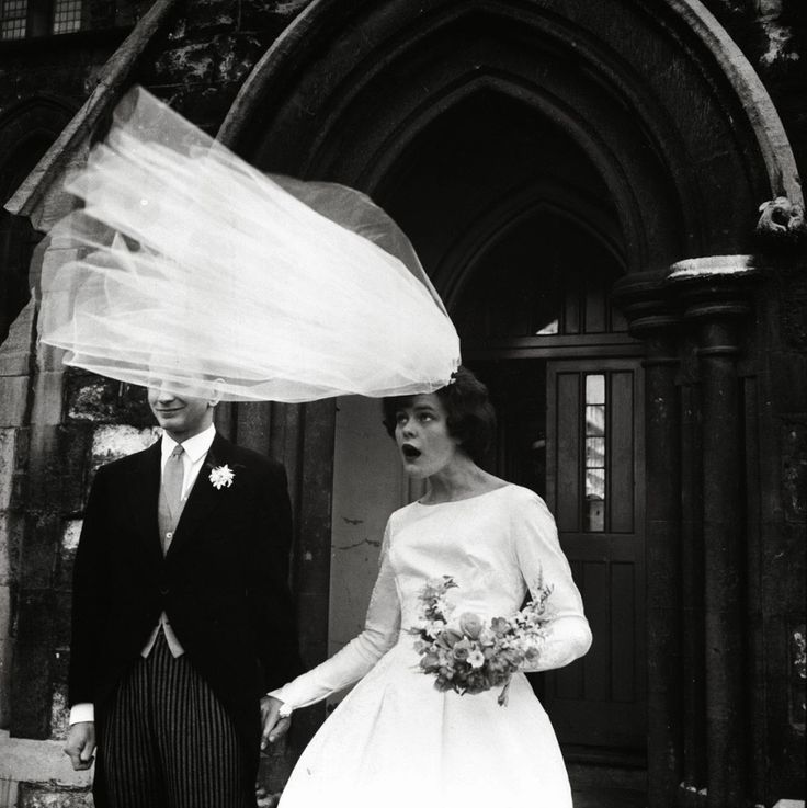 a man and woman dressed in formal wear holding hands while walking down the street with an umbrella over their heads