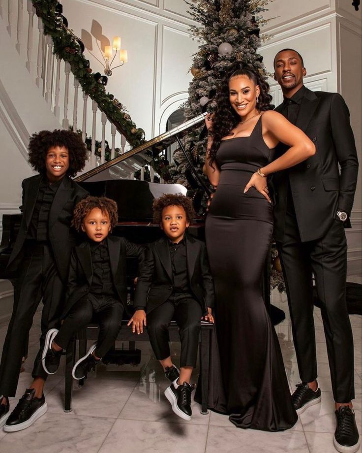 a group of people standing next to each other in front of a christmas tree and piano