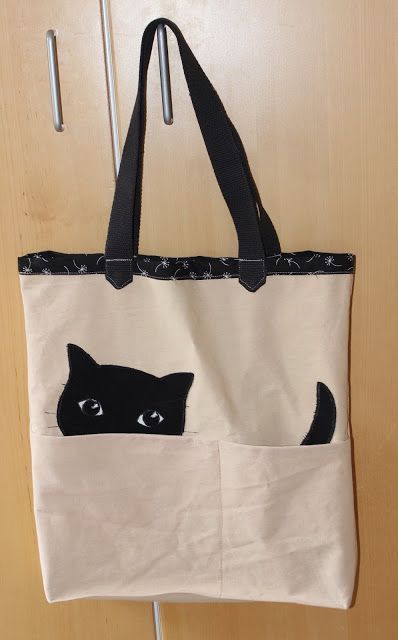 a black and white cat in a pocket on a tote bag hanging from a hook