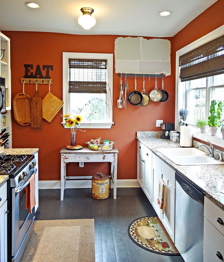 a kitchen with an orange wall and white cabinets has sunflowers on the window sill