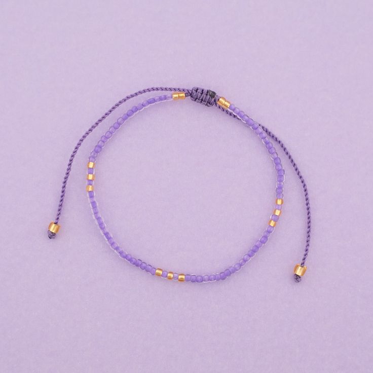 a purple beaded bracelet with gold beads on a lavender background and a small yellow bead