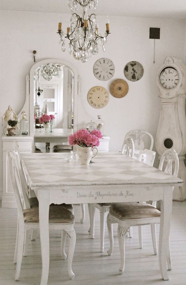 a white dining room table with chairs and clocks on the wall above it, in front of a mirror