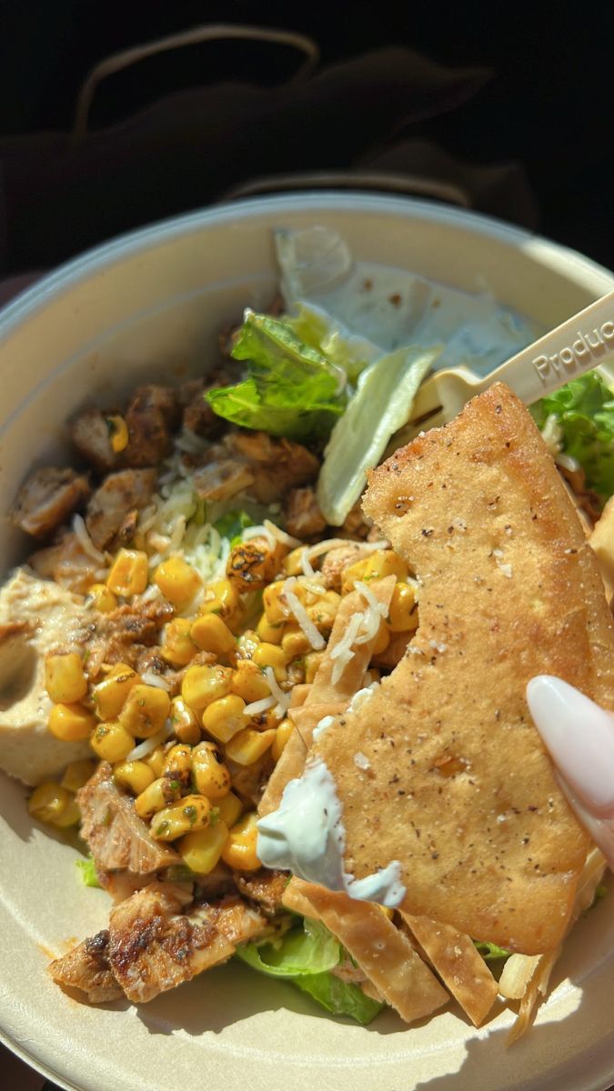 a person is holding a fork over a plate of food that includes corn, lettuce and tortilla chips