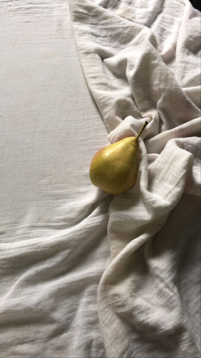 a pear laying on top of a white sheet covered in linens and sheetstuffs