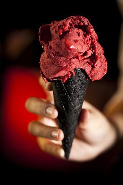 a person holding an ice cream cone in their hand with red icing on it