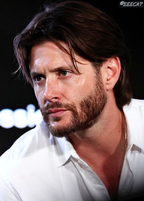 a man with long hair and beard wearing a white shirt looking off to the side