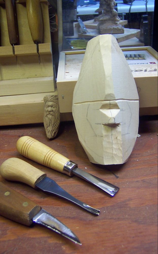 carving tools are sitting on a table next to a carved head and knifes in front of it