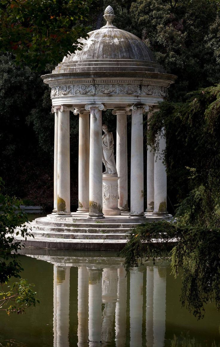 a statue in the middle of a pond surrounded by trees