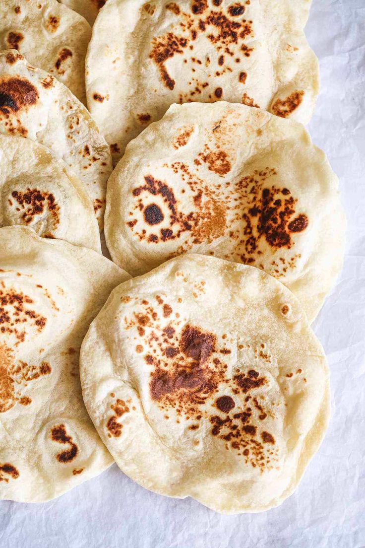 six pita breads are arranged in a circle on a white tablecloth with brown sprinkles