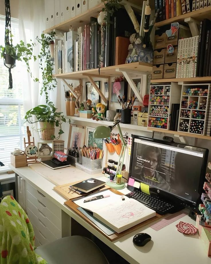 a desk with a computer, books and plants on it in front of a window