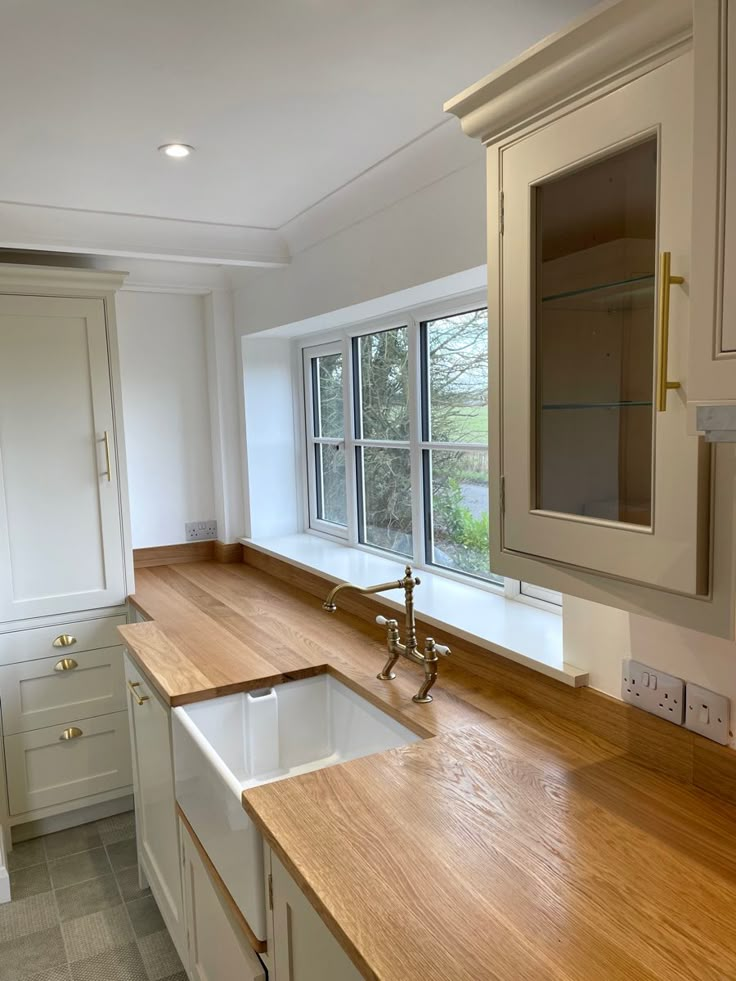 an empty kitchen with white cabinets and wood counter tops in front of a large window