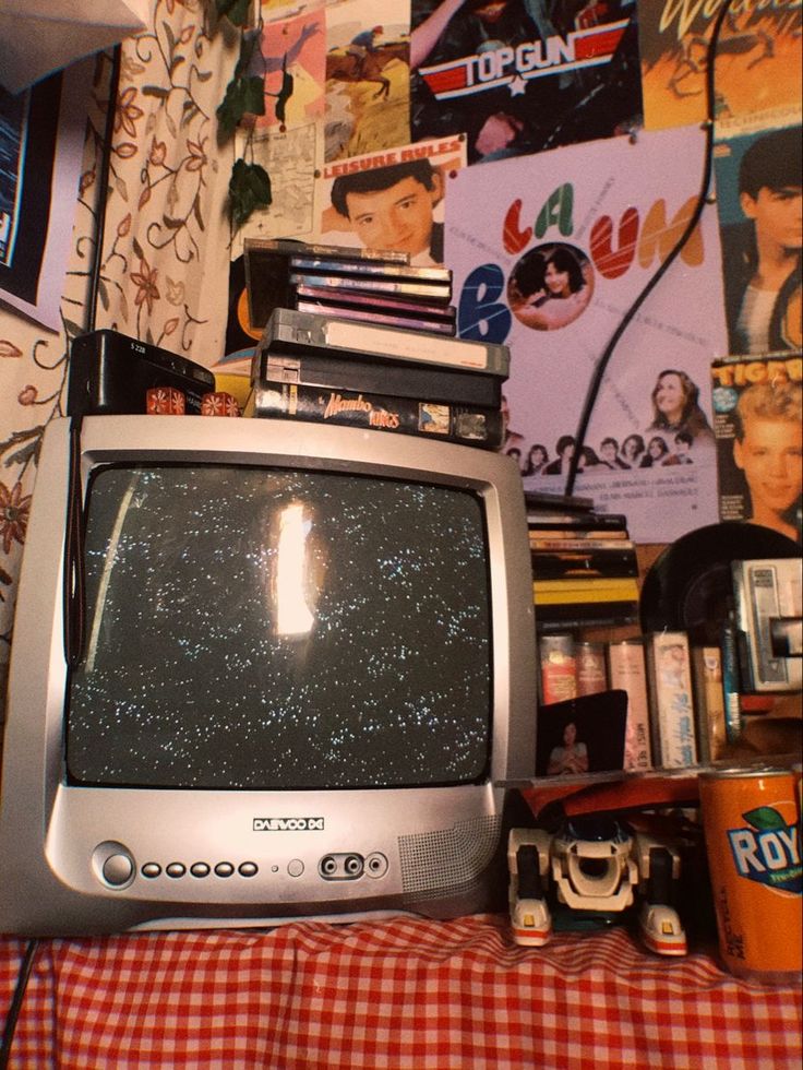 an old tv sitting on top of a table in front of a wall covered with posters