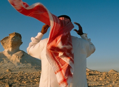 a man standing in the desert with his hands up to his head and arms outstretched