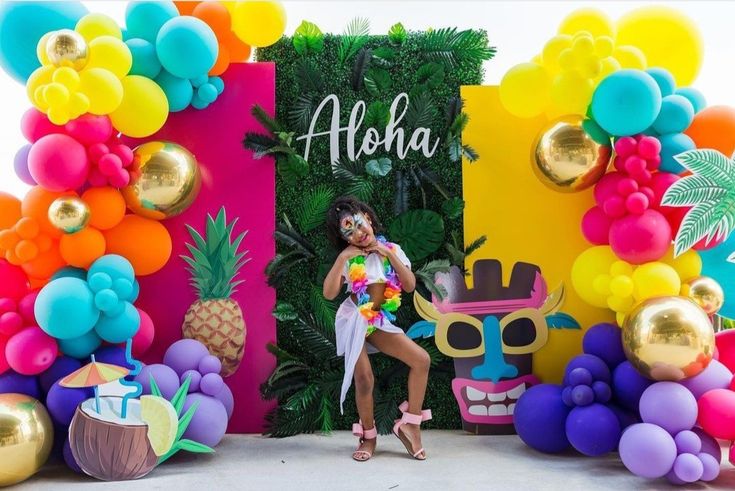 a woman standing in front of a backdrop with balloons and pineapples on it