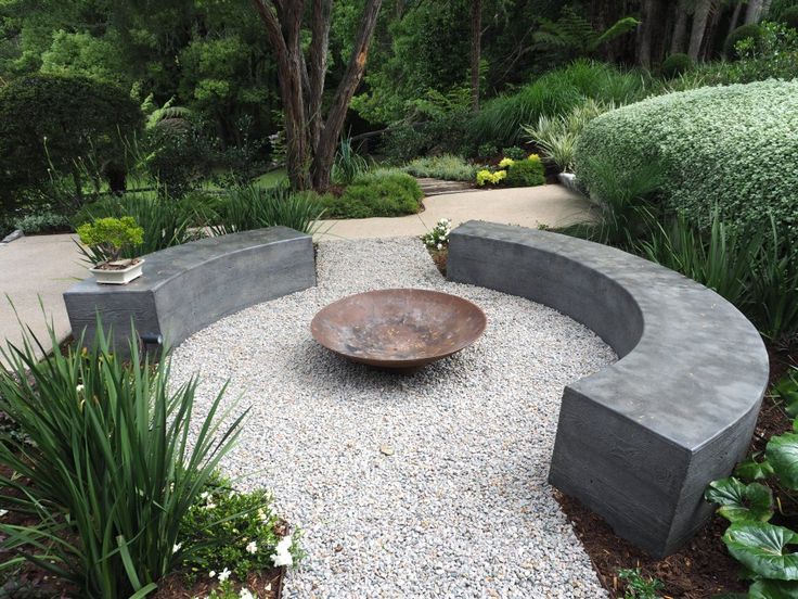 a circular bench sitting in the middle of a graveled area surrounded by plants and trees