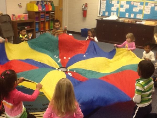 children are sitting on the floor and playing with a large parachute in a class room