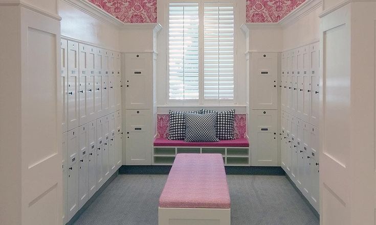 a pink bench sitting in the middle of a room filled with lockers and drawers