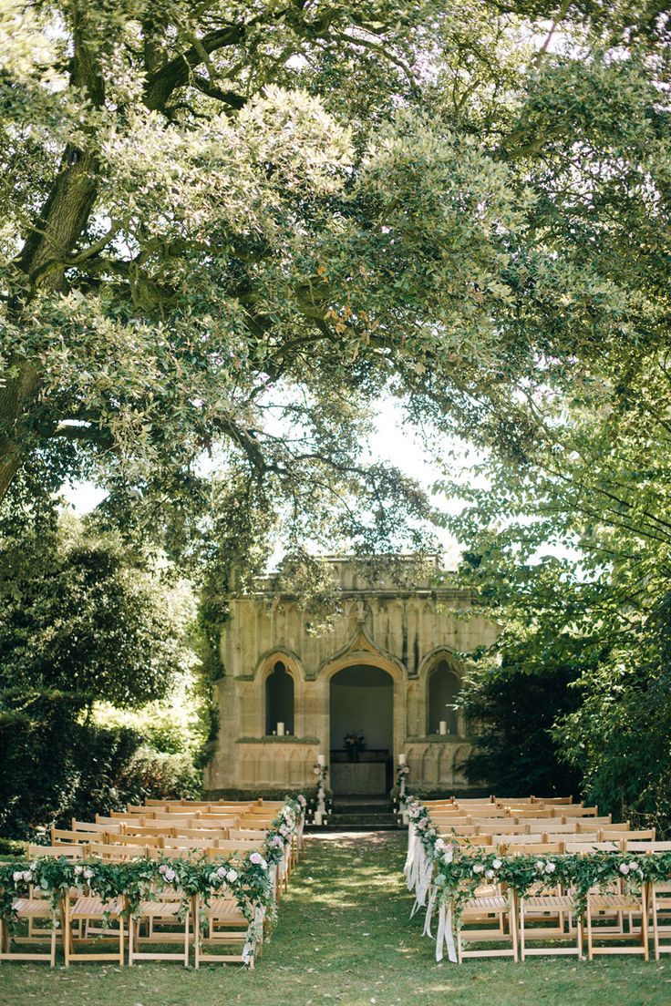 an outdoor ceremony set up with wooden chairs and greenery on the lawn, surrounded by trees