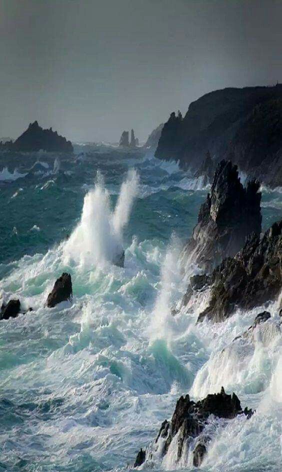 waves crashing on rocks in the ocean with dark clouds above them and blue water below