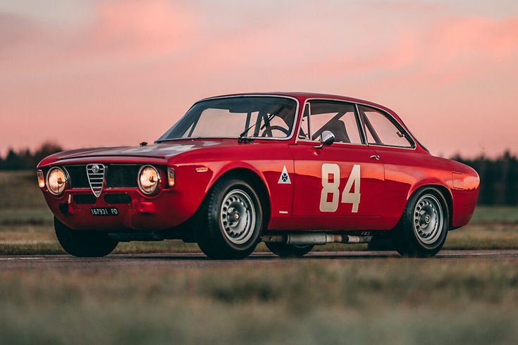 an old red sports car is parked on the road