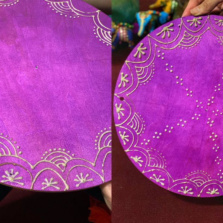 two purple plates with designs on them being held up by someone's hands,