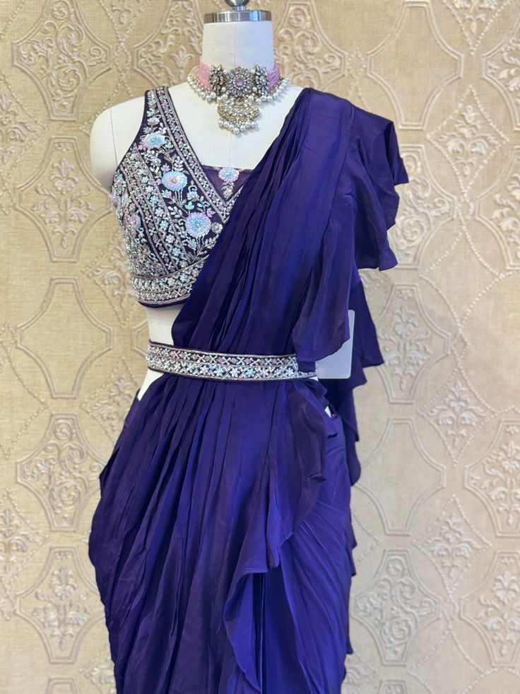 This deep purple ruffled saree exudes elegance with its cascading layers, paired with a heavily embellished blouse and a matching belt. Perfect for weddings and festive occasions, it blends traditional charm with a modern touch. Key Features: Color: Deep Purple Design: Ruffled saree with a fully hand-embellished blouse Accessories: Matching belt for a defined silhouette Occasion: Ideal for weddings, festive events, and grand celebrations Elegant Pre-draped Saree With Ruffles For Navratri, Traditional Wear With Ruffles And Traditional Drape, Designer Wear Saree With Ruffles In Traditional Drape, Designer Wedding Pre-draped Saree With Dupatta, Traditional Ruffled Choli For Designer Wear, Traditional Designer Choli With Ruffles, Elegant Purple Pre-draped Saree, Purple Pre-draped Saree With Cutdana For Party, Festive Purple Pre-draped Saree For Wedding