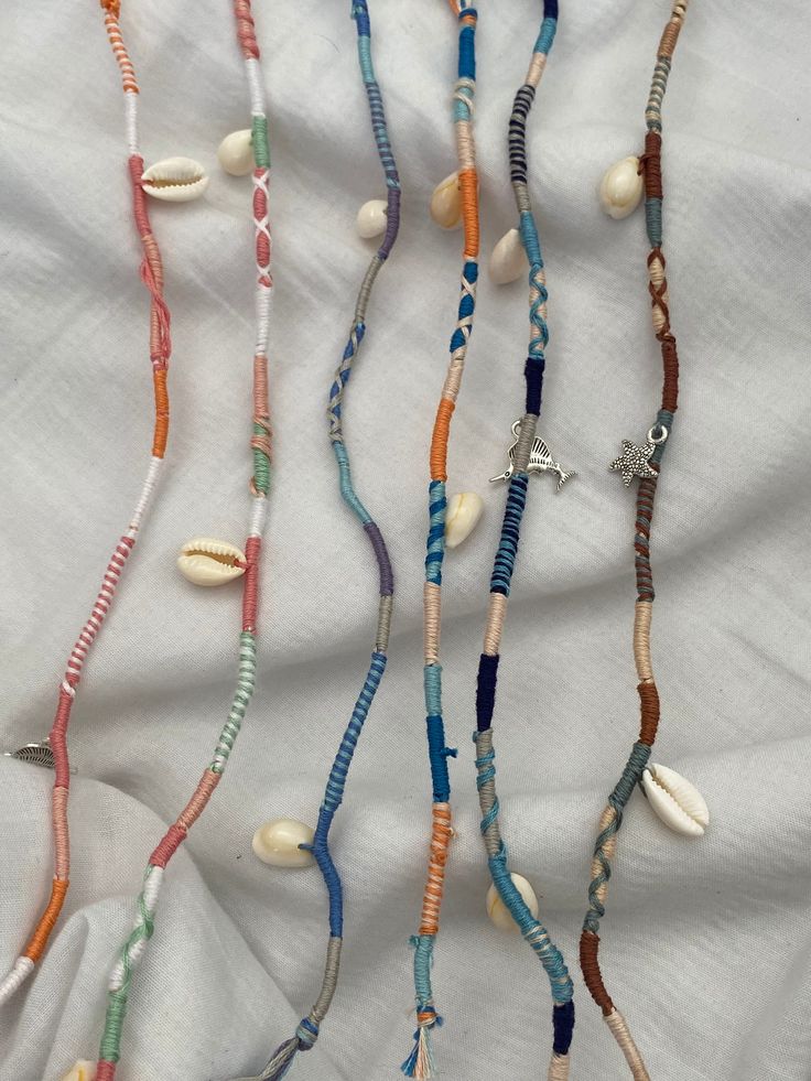 several necklaces are displayed on a white cloth with shells and beads hanging from them