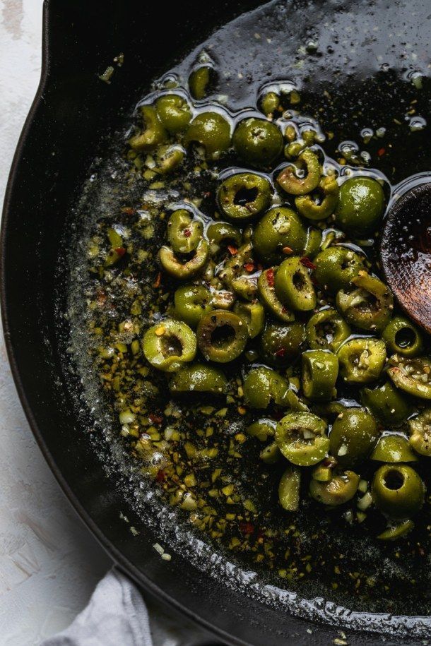 green olives being cooked in a skillet with seasoning and pepper flakes