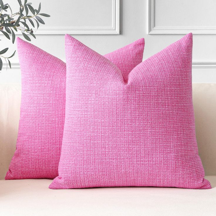 two pink pillows sitting on top of a couch next to a potted green plant