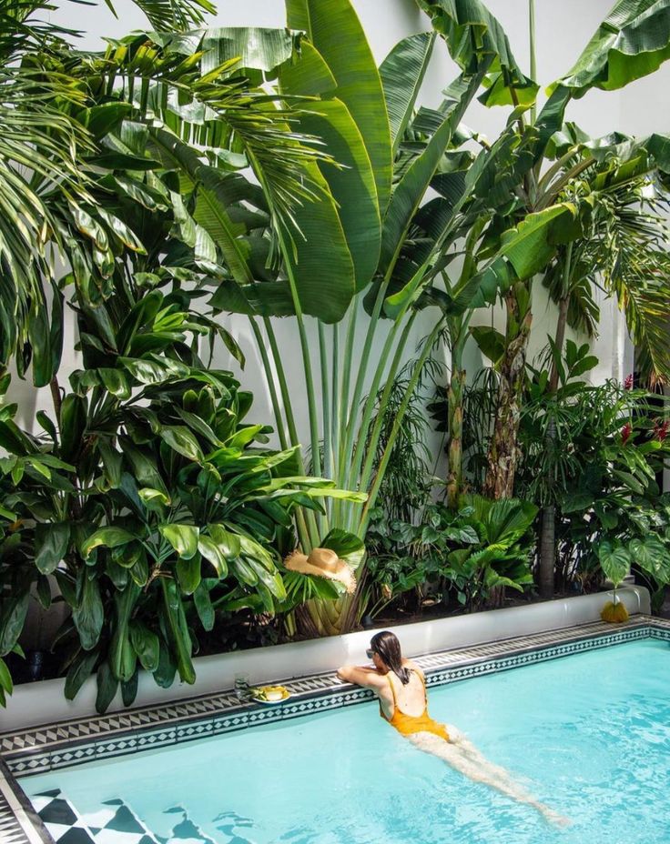 a woman in a yellow swimsuit is swimming in a pool surrounded by tropical plants