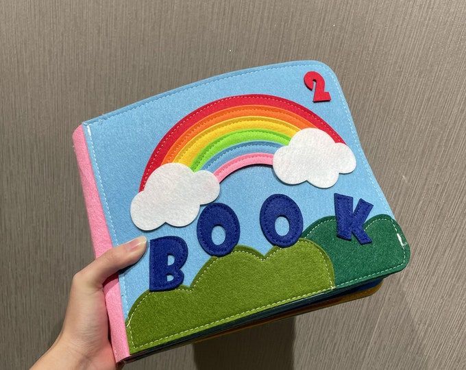 a hand holding up a book with a rainbow on the front and number 2 on the back