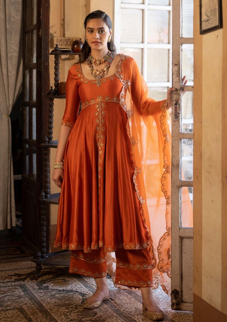 Editor's Note Presenting an exquisite rust chiniya silk anarkali set, beautifully paired with a tissue base dupatta adorned with antique gold zari and resham embroidery. The rust chiniya silk f... Elegant Anarkali Suits, Tissue Anarkali Dress, Embroidery On Orange Fabric, Tissue Fabric Dress Design, Silk Dresses Indian, Rust Orange Lehenga, Mehndi Gharara, Wedding Guests Outfits, Elia Martell