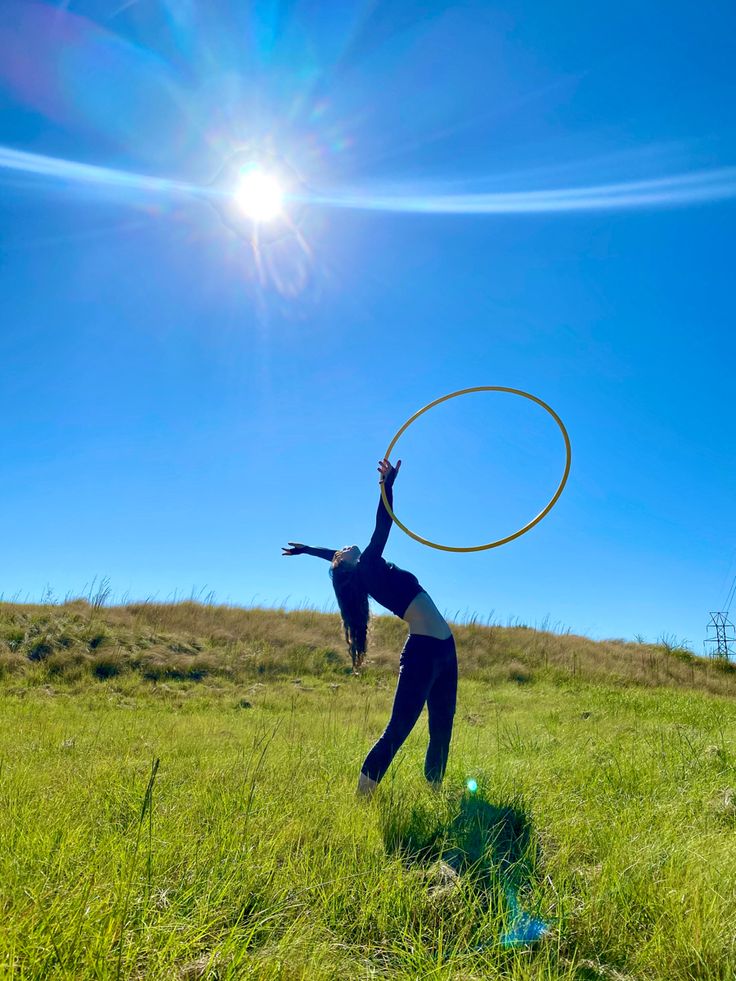 a woman is playing with a hula hoop in the grass on a sunny day