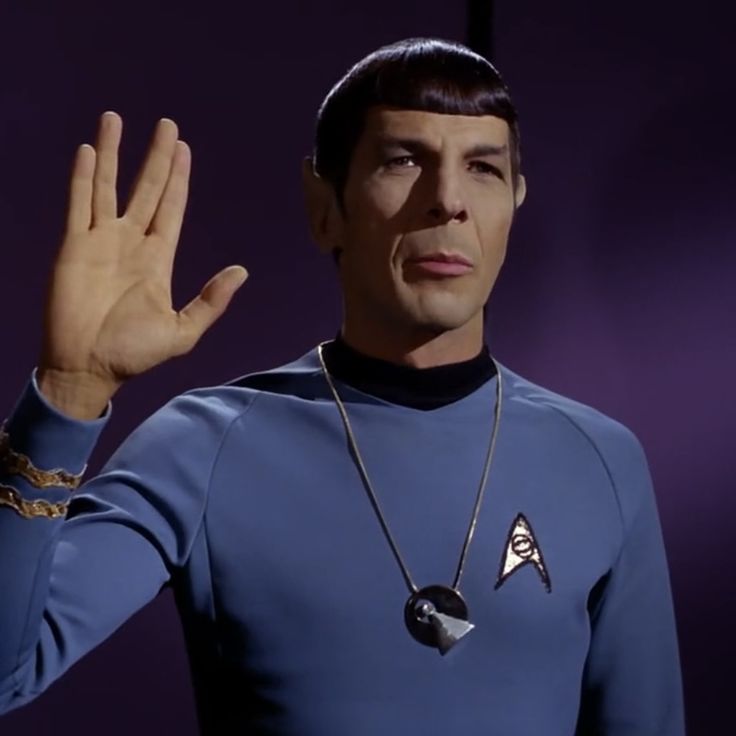 a man in a blue shirt holding his hand up to the side while wearing a star trek uniform