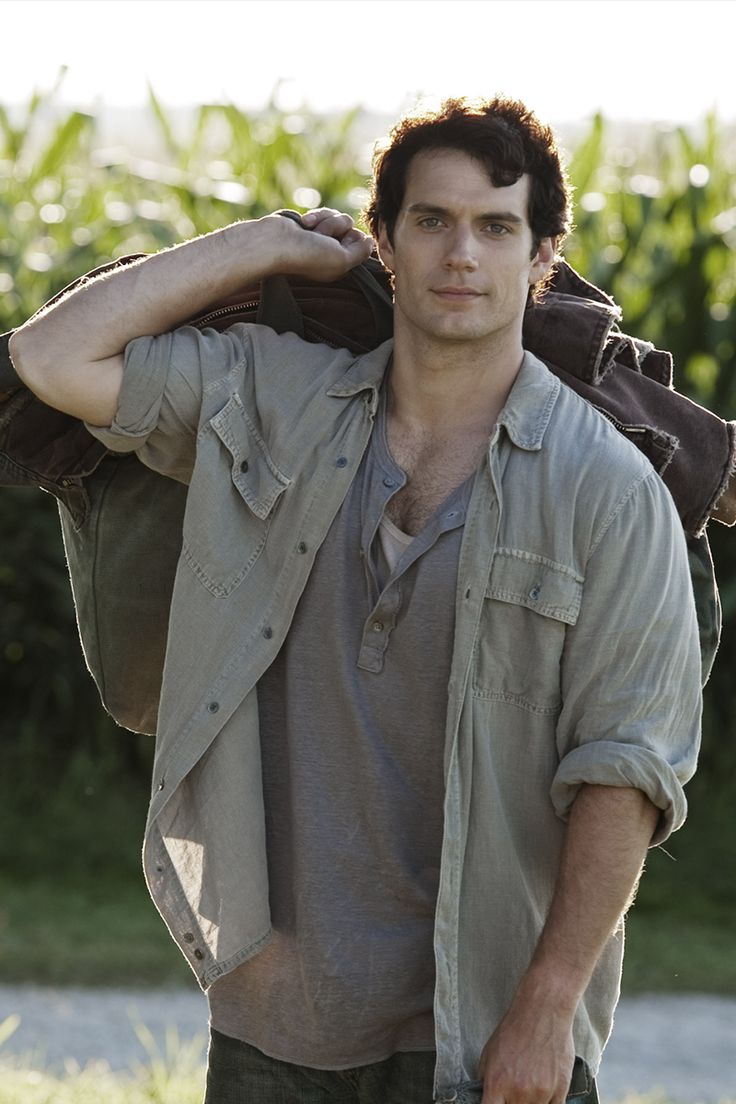 the young man is carrying his jacket over his shoulders while walking through the grass in front of some trees